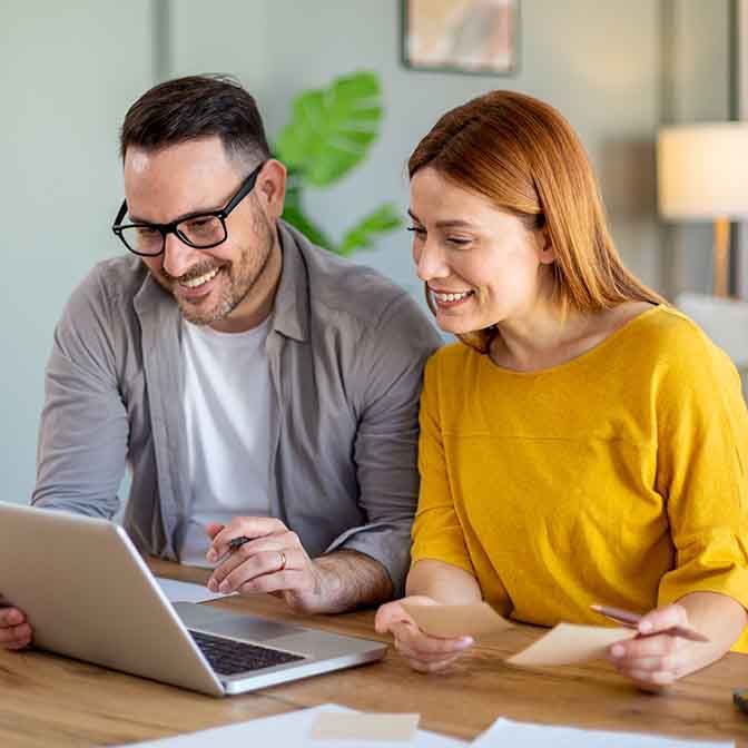 Happy smiling couple sitting together at home table with laptop.