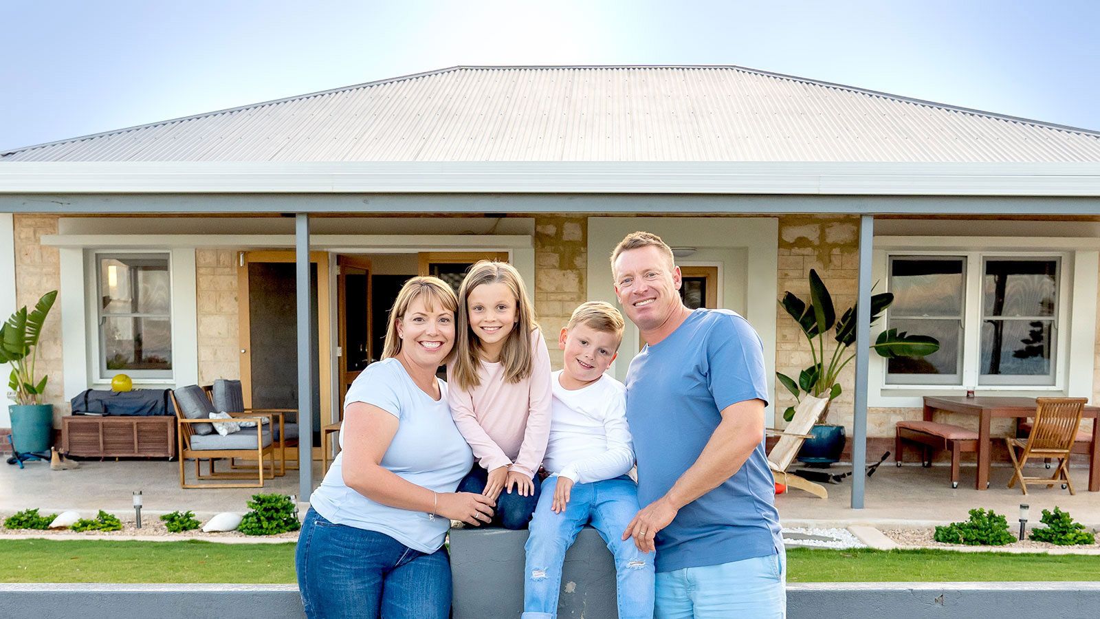 A family of four posing in front of their ranch style home