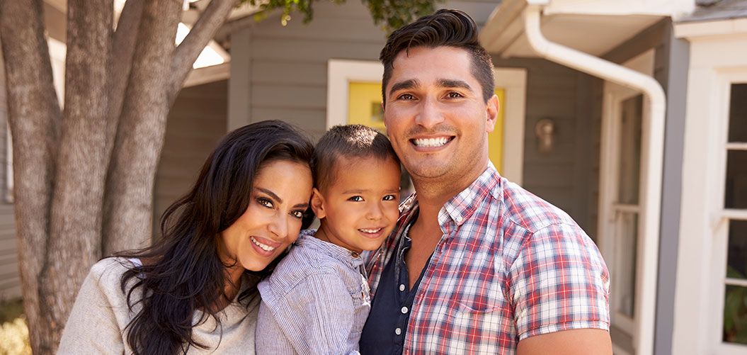 Young Hispanic family standing in front of their home.