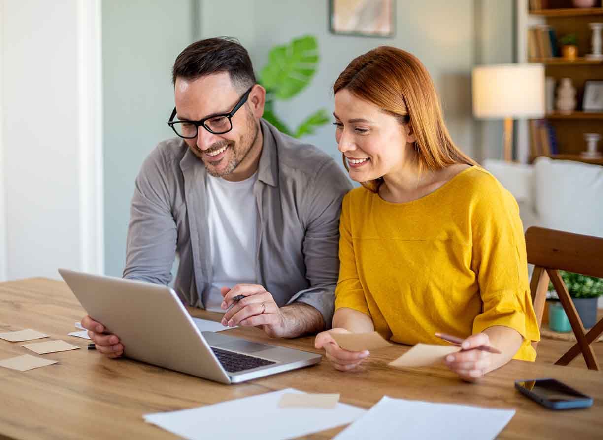 Happy smiling couple sitting together at home table with laptop.