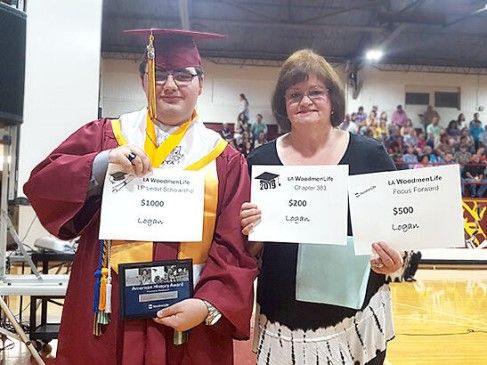 A young man in a cap and gown poses with a woman; both are holding awards.