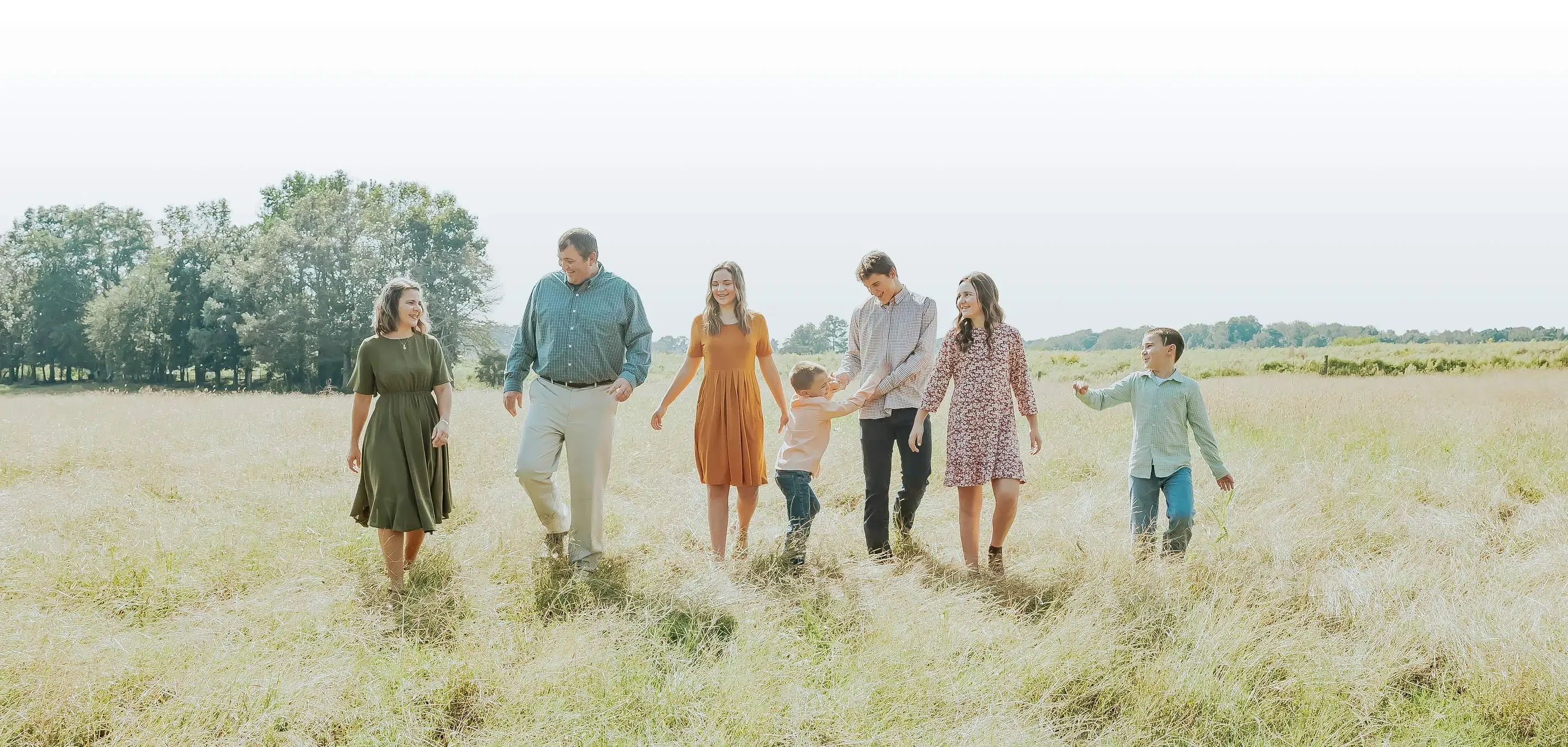 A lighthearted family strolls through a grassy field on a bright and sunny day