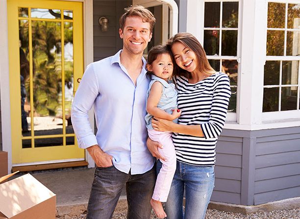 A father and mother holding their child in front of a house. 