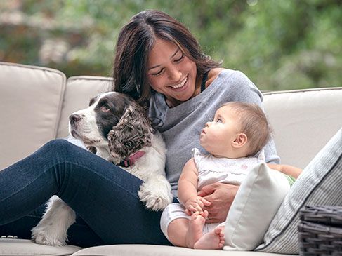 A mom sitting with her baby and dog on the couch.
