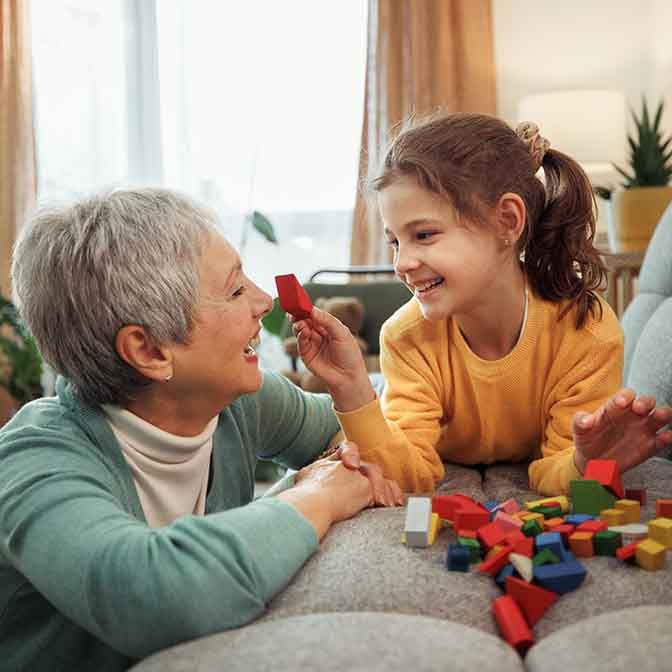 Grandmother and granddaughter enjoy playful moments together, building with wooden toy blocks in their home