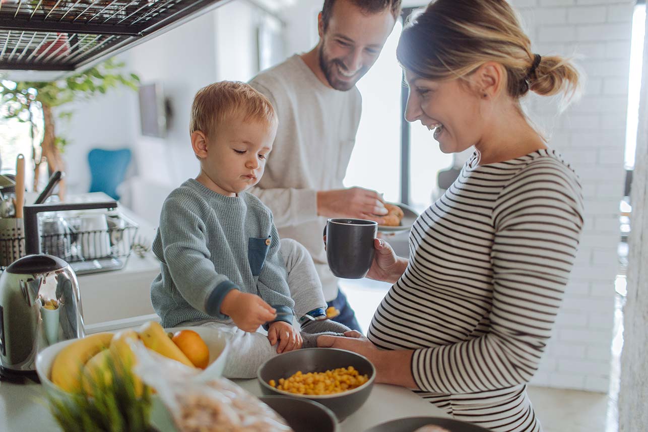 Young couple standing together enjoying breakfast with their infant son who is seated on the counter
